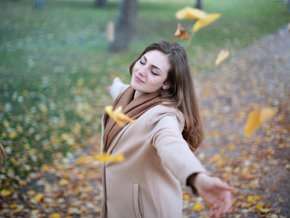 Woman twirling looking happy in falling leaves
