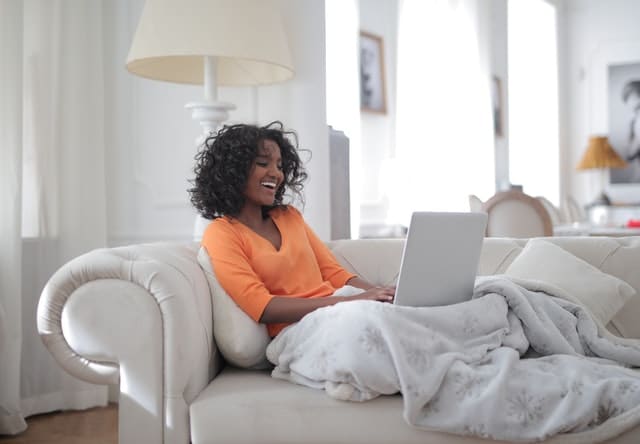 woman curled up on couch in cozy blanket on computer laughing, habits for health